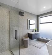 A modern bathroom with a large walk in shower, frameless glass panels, tiled walls, and soft natural lighting.