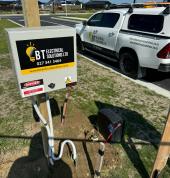 An outdoor electrical installation setup featuring BT Electrical Solutions signage, tools, and a work vehicle parked nearby.